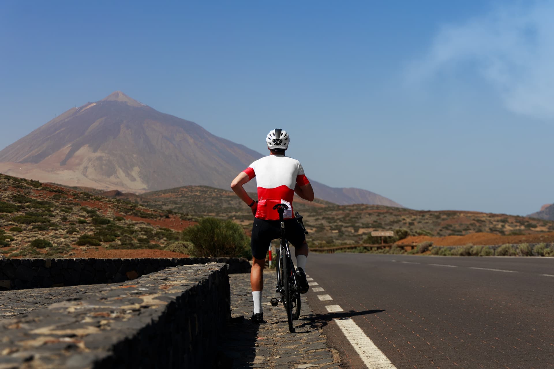 Cyclist with bicycle pauses by a road overlooking a large mountain in Tenerife.